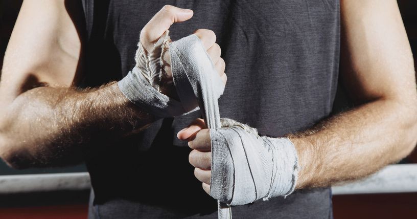 Strong man wrap hands on black background. Man is wrapping hands with boxing wraps, ready for training and active exercise